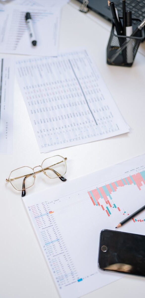 Flat lay of business documents with magnifying glass, glasses, and smartphone on a desk.